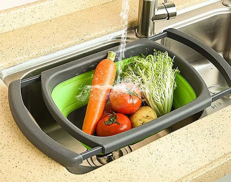 Passoire pliable en silicone sous un robinet, contenant des légumes, avec poignées réglables pour une cuisine mobile et le camping.