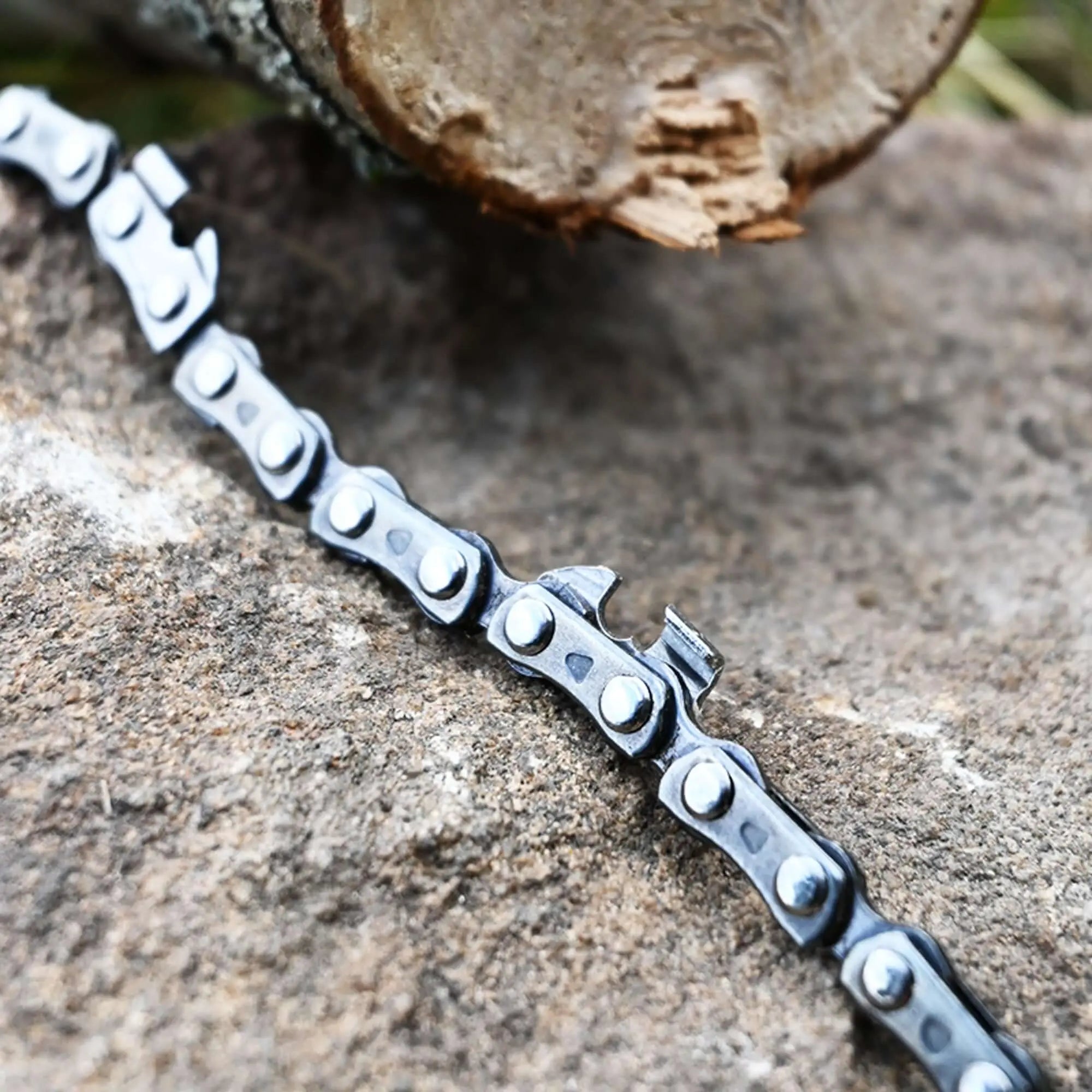Close-up of a portable manual camping chainsaw chain on rock with wood, highlighting robust design for efficient wood cutting.