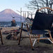 Chaise de camping pliable en bois noir près d'un feu de camp, avec vue sur une montagne au loin, parfaite pour les activités de plein air.