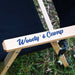 Gros plan sur une chaise de camping en bois noir pliable avec le texte "Woody's Camp", posée sur une pelouse à l'extérieur.
