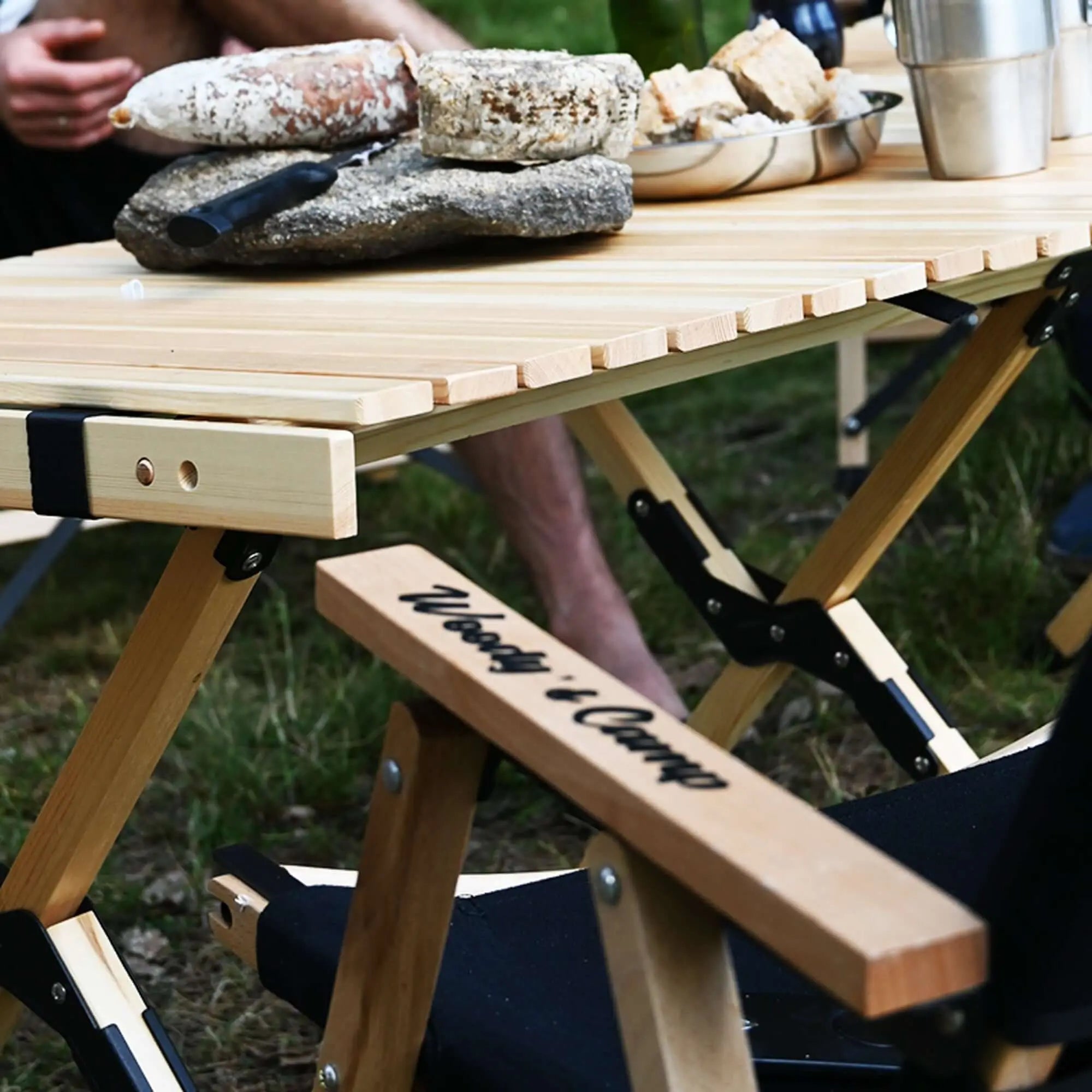 Outdoor picnic with a portable wooden camping table and chair, showcasing rustic snacks and beverages in a natural setting.