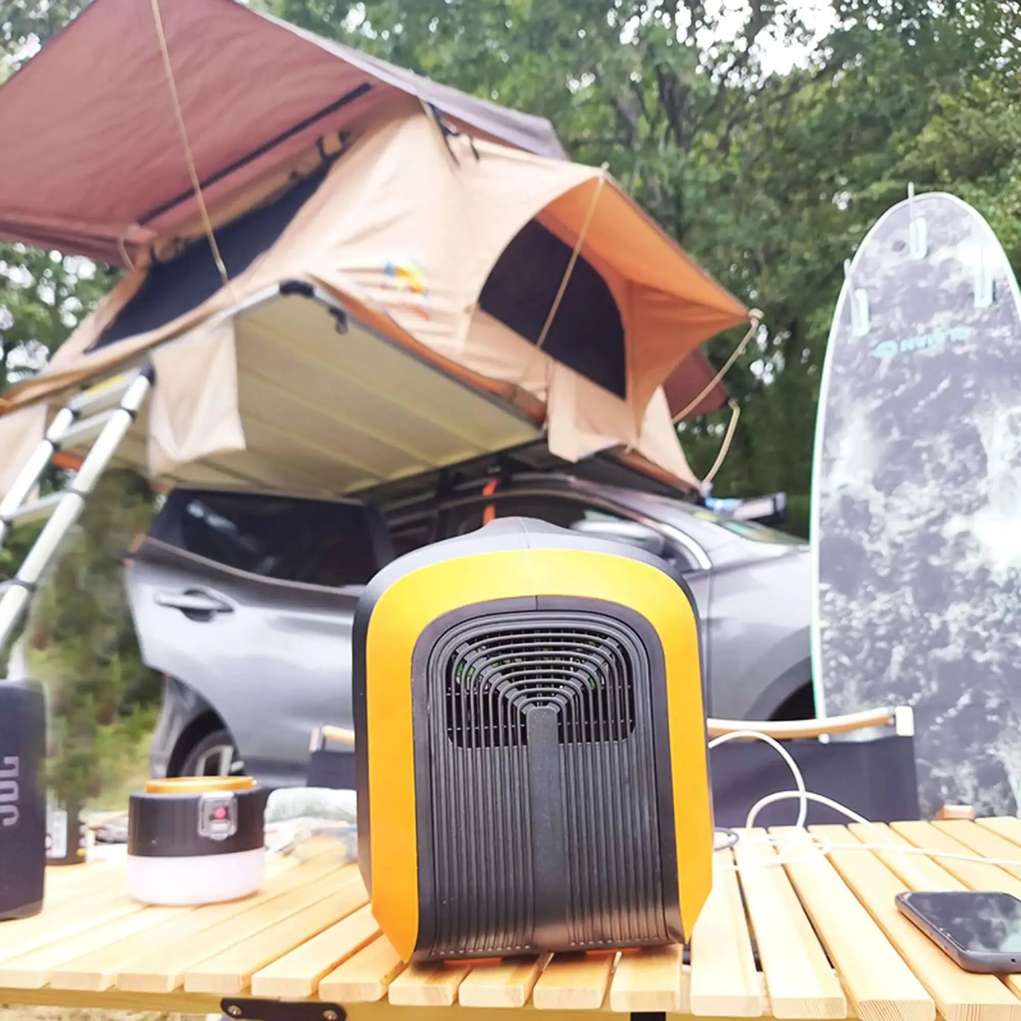 Portable 1200WH power station with solar panels on outdoor camping setup with rooftop tent and surfboard.
