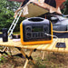 Station d'énergie portable avec des panneaux solaires sur une table de camping, illustrant l'utilisation en extérieur pour charger des appareils.