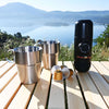 location louer une Machine à café expresso portable avec deux tasses en acier inoxydable et des capsules sur une table de pique-nique surplombant un lac et des montagnes pittoresques.