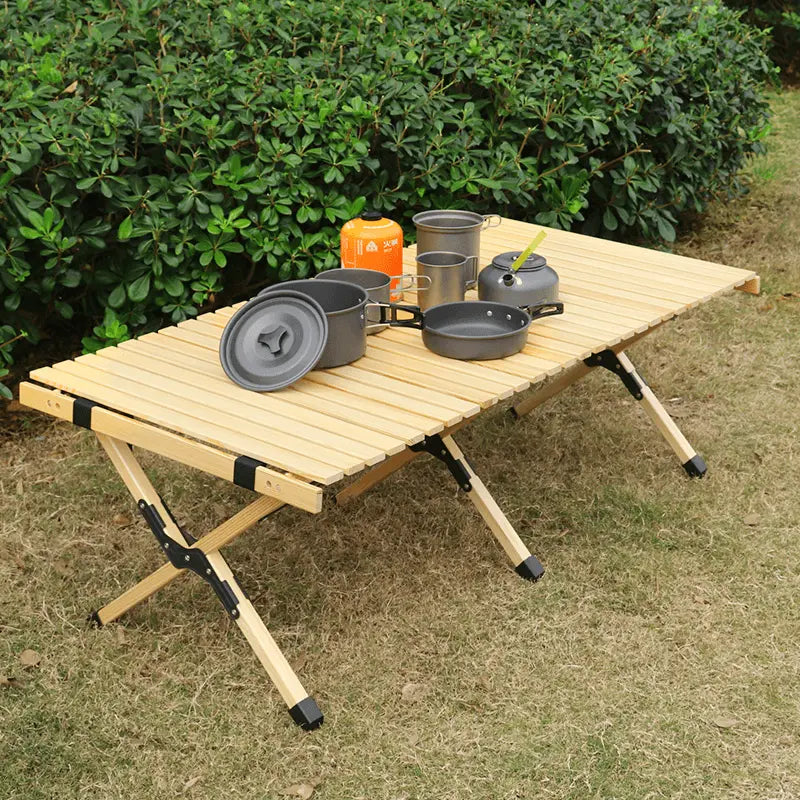 Pliable wooden camping table set with pots and pans, shown outdoors. Folds for easy storage and supports 4 to 6 people.