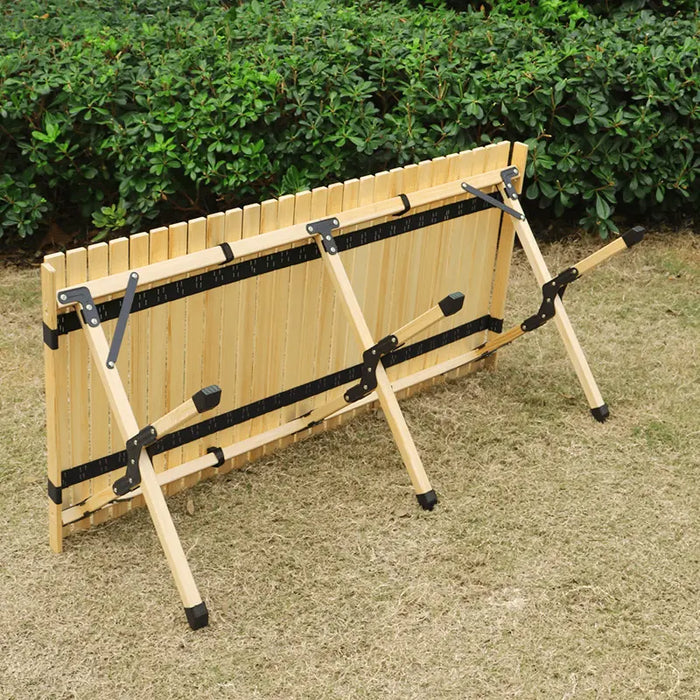 Table de camping en bois pliable avec des charnières noires posée sur de l'herbe, mettant en avant un design compact pour un rangement et un transport faciles.