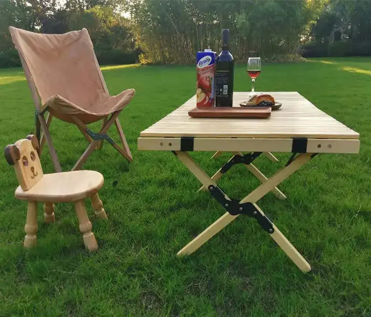Pliable wooden camping table set up outdoors with chairs, drink, and food, showcasing durable design for comfortable outdoor dining.