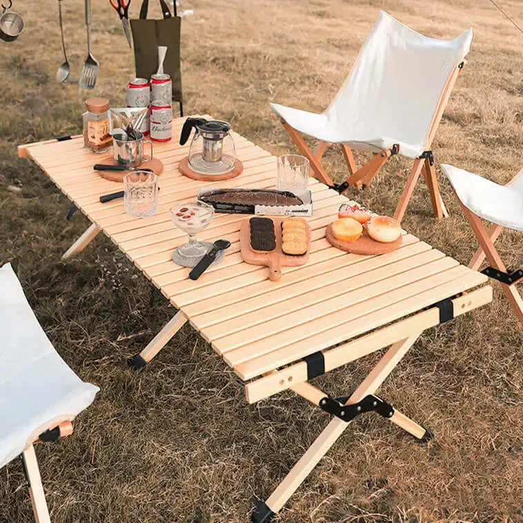 Table en bois pliable pour camping, dressée pour un repas en plein air, avec tabourets pliants et ustensiles de cuisine.