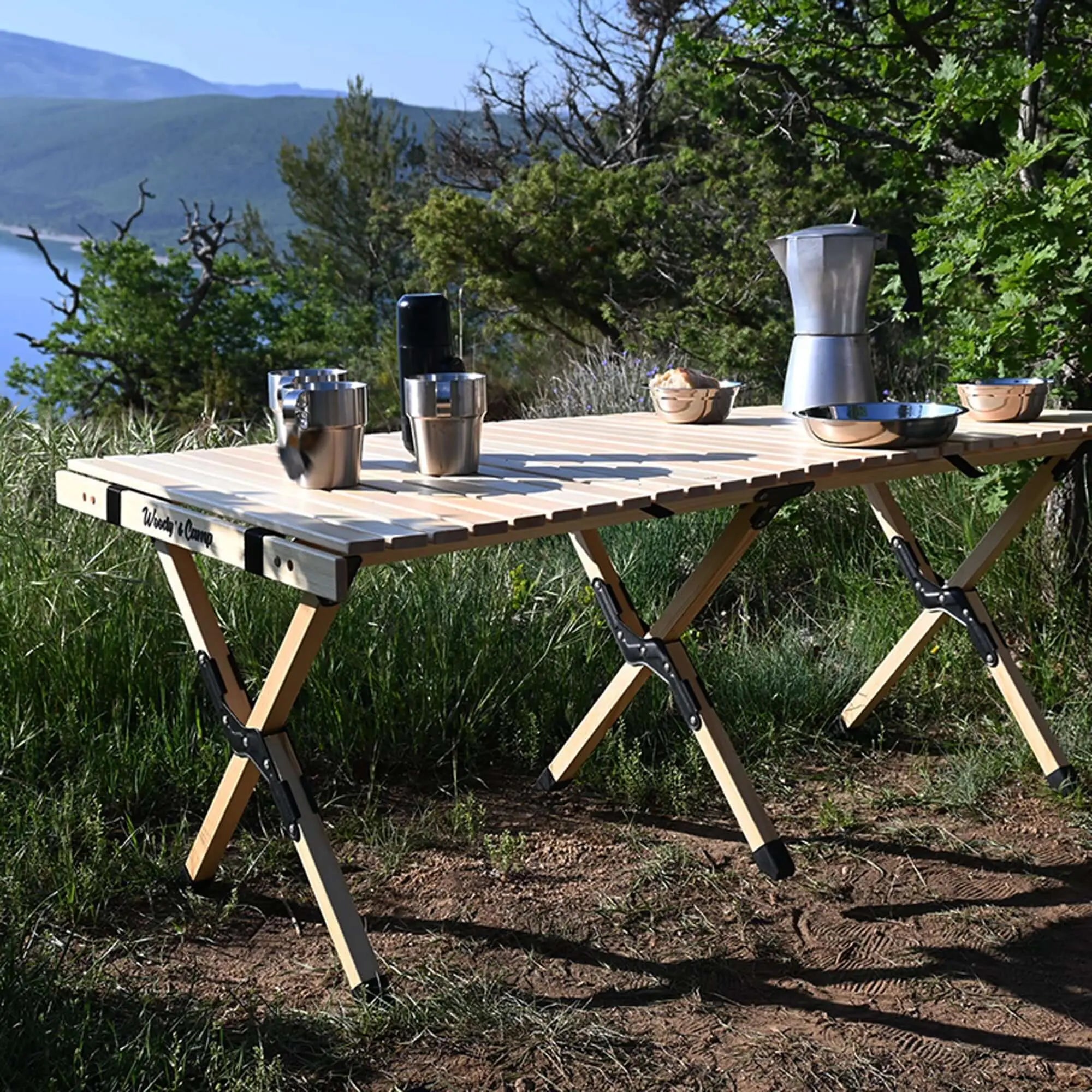 Foldable wooden camping table with dishes and coffee pot in a scenic outdoor setting, designed for convenience and durability.