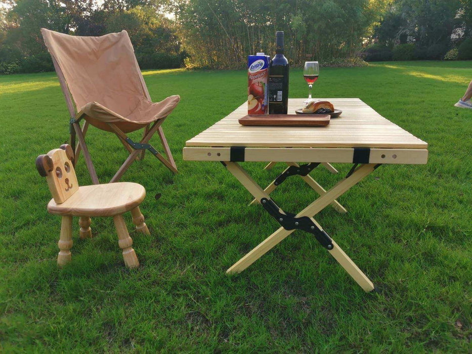 Table en bois pliable pour le camping avec accessoires de pique-nique sur gazon, entourée de chaises pliantes, idéale pour des repas en plein air.