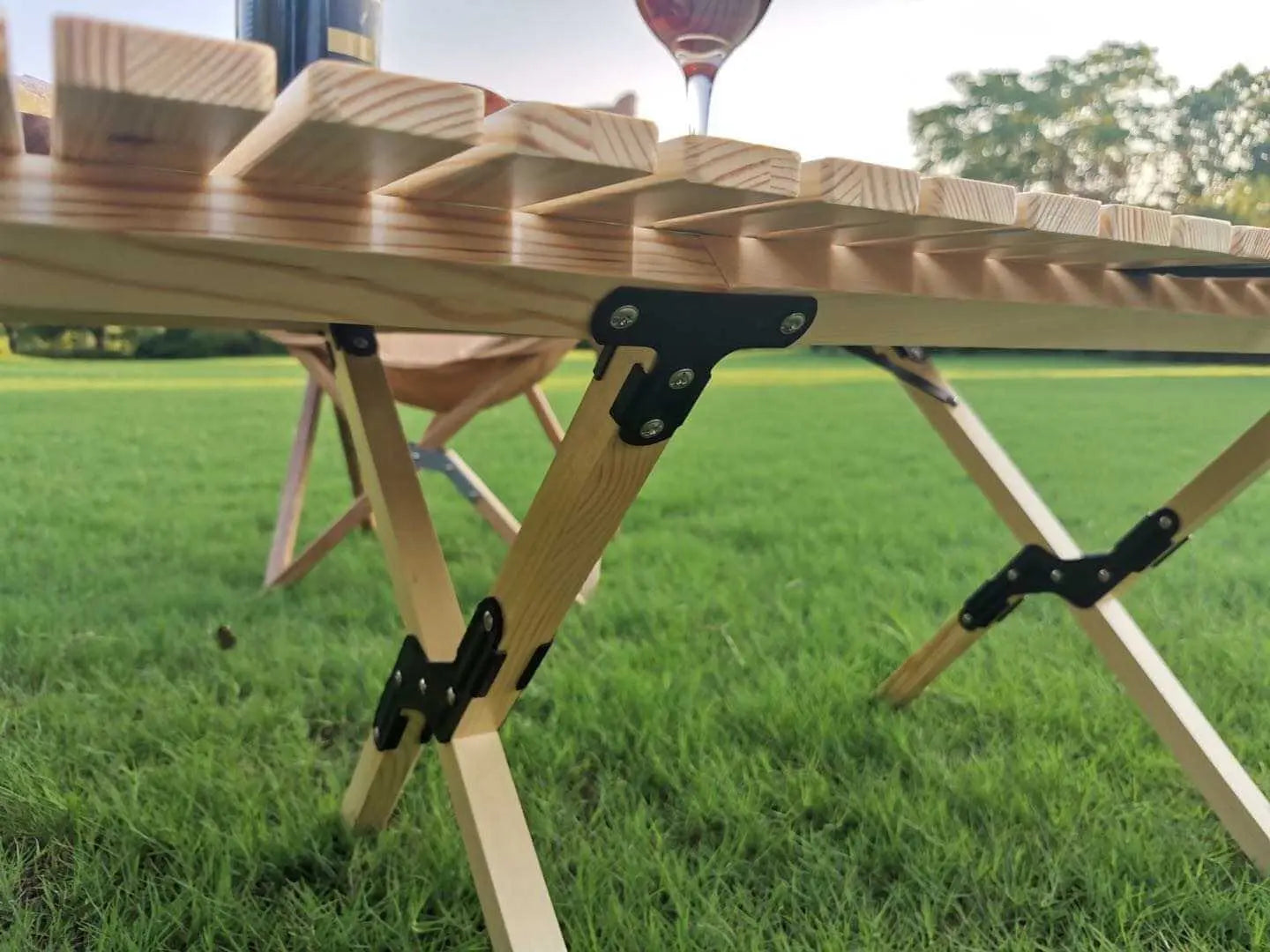 Wooden folding camping table with sturdy hinges, set up on grass, showcasing durability and portability features for outdoor use.