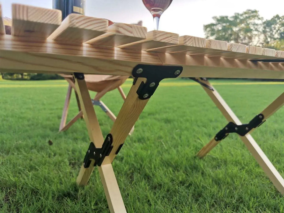 Table de camping pliable en bois avec des charnières solides, installée sur l'herbe, mettant en avant ses caractéristiques de durabilité et de portabilité pour une utilisation en extérieur.