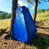 Tente de douche extérieure pliante bleue installée dans une forêt, offrant de l'intimité pour prendre des douches, se changer et plus encore lors des aventures.