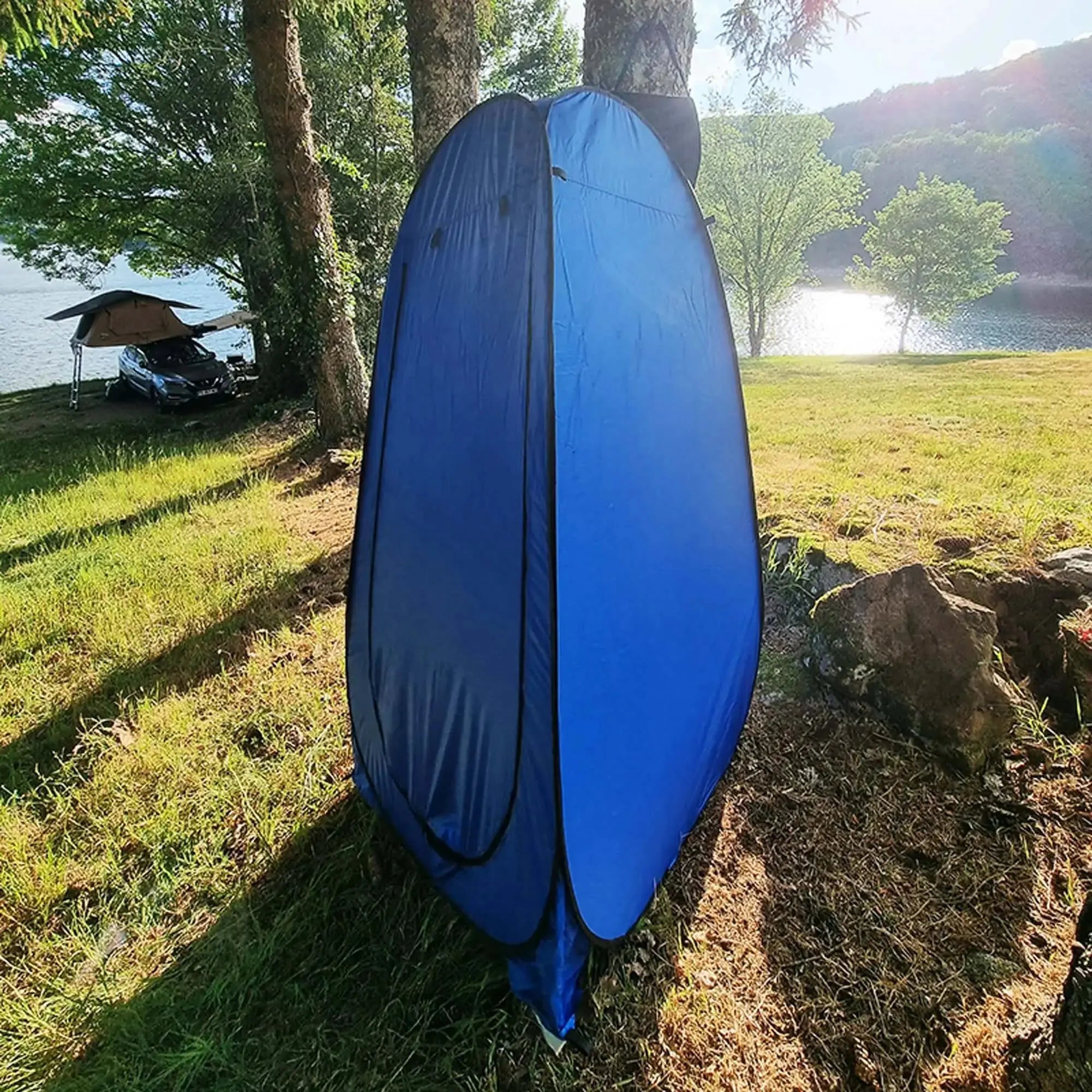 Tente de douche camping en plein air pliable bleue installée près d'un lac, idéale pour voyage et aventure.