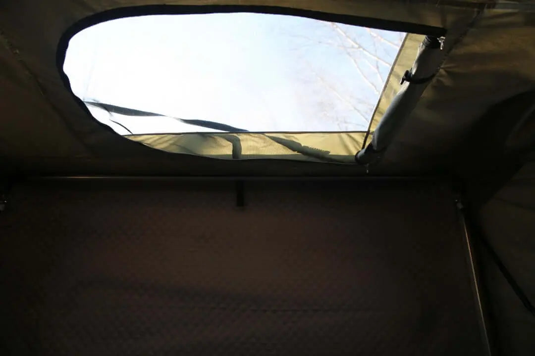 Interior view of a rigid roof tent rental, featuring a partially opened window with a sky view, suitable for 4-5 people.