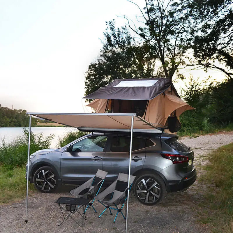 Car with rooftop tent and retractable awning by a lake, providing shelter and comfort for camping in nature.